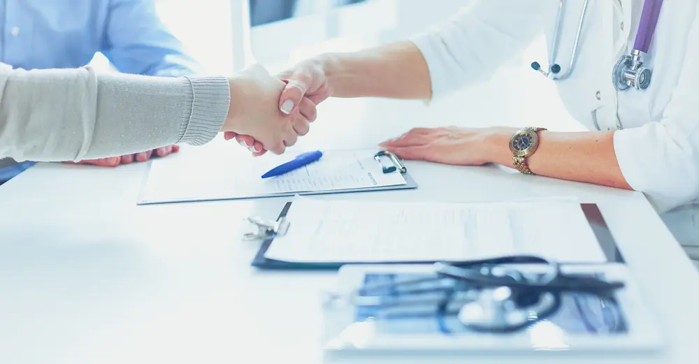 Two people shaking hands over a table with medical equipment.